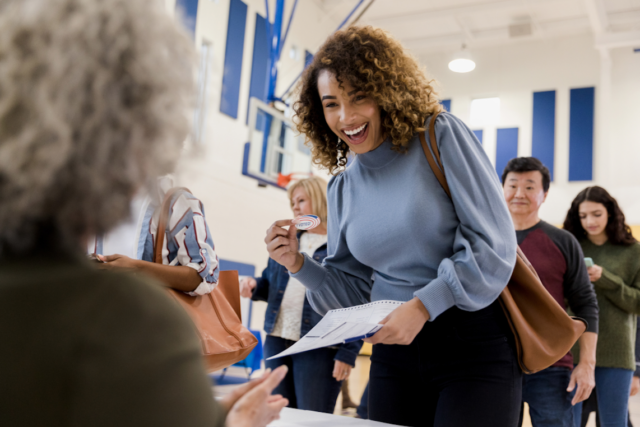 Picture of a smiling Black young female who is handing in her voting ballot